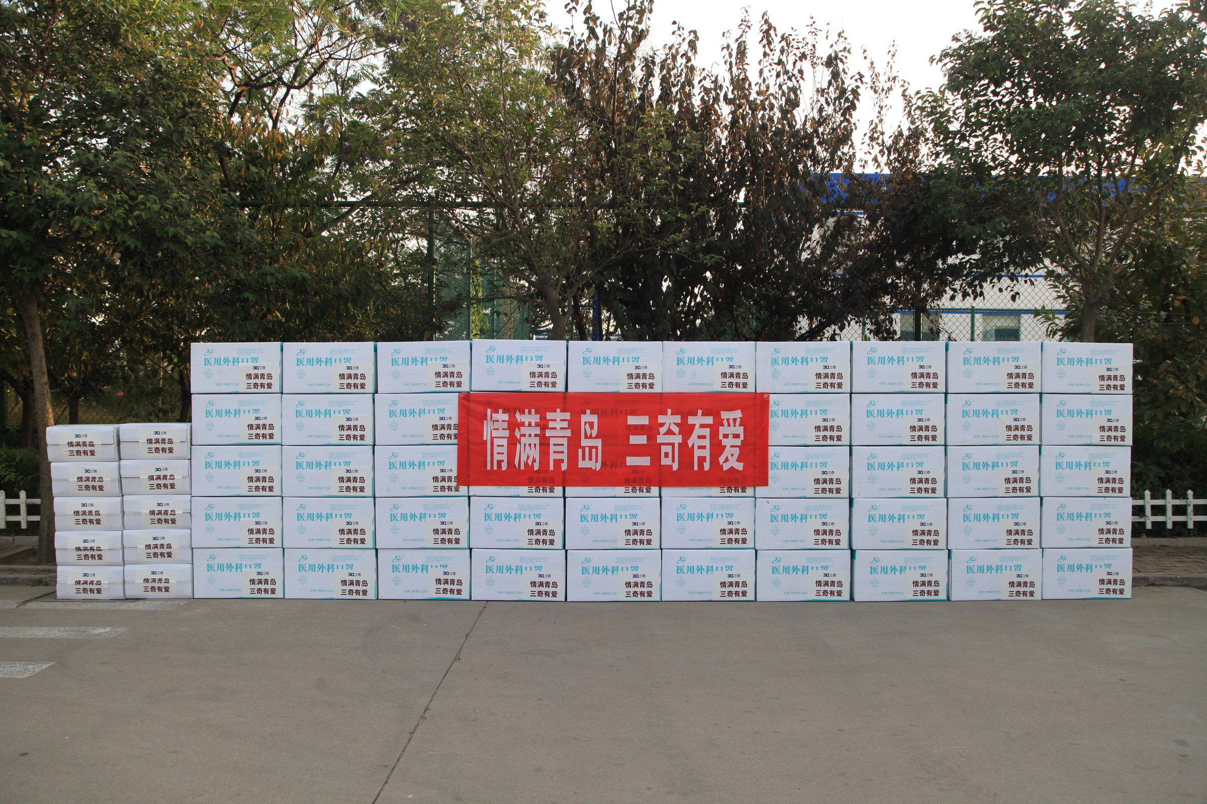 Boxes of donated supplies arranged behind a Qingdao support banner